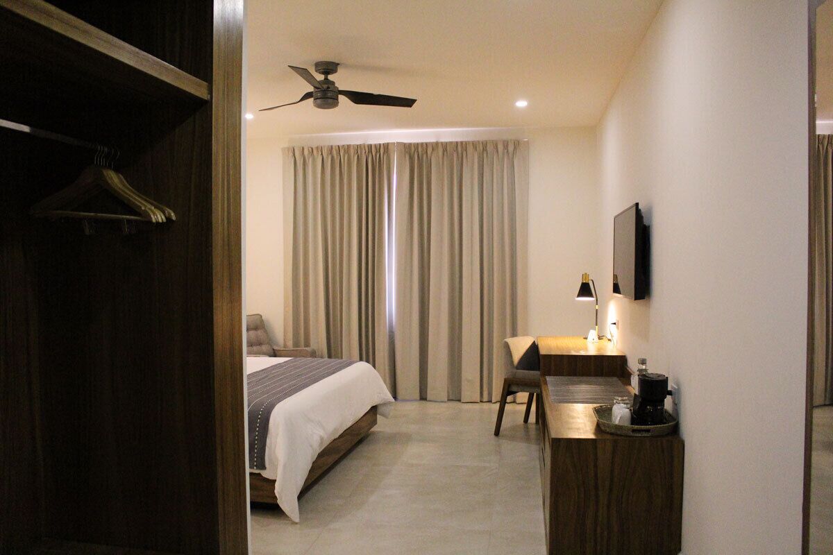 A hotel room with a bed, a desk, a chair, a coffee maker, a ceiling fan, and a TV.
