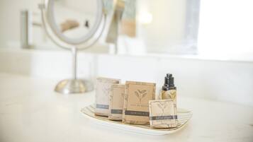 Un tocador de baño con espejo, lavamanos y una bandeja con diversos artículos de aseo, incluyendo un kit de costura, jabón de baño y una botella de champú.