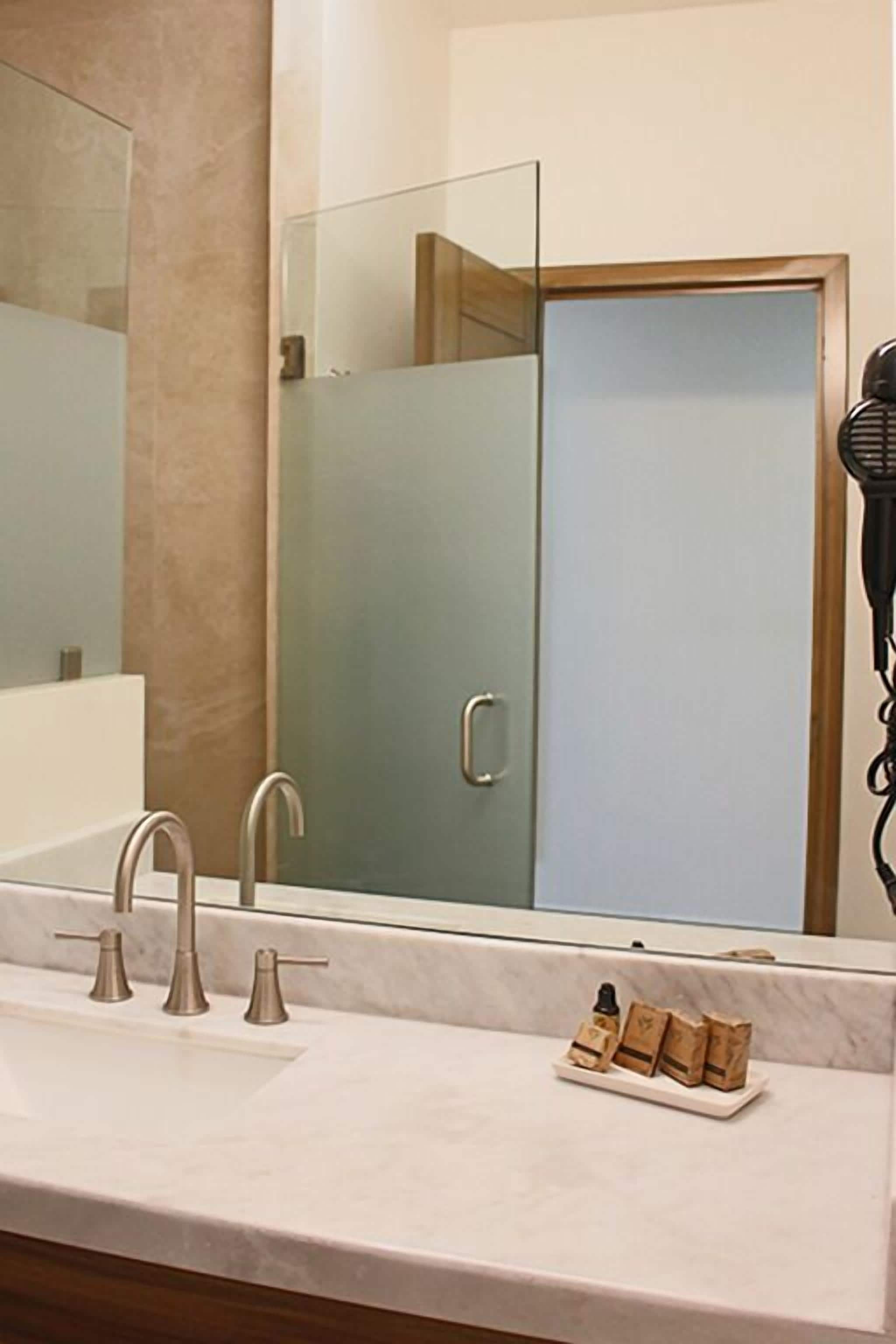 A bathroom with a large mirror, a sink with two faucets, and a hairdryer on the wall.