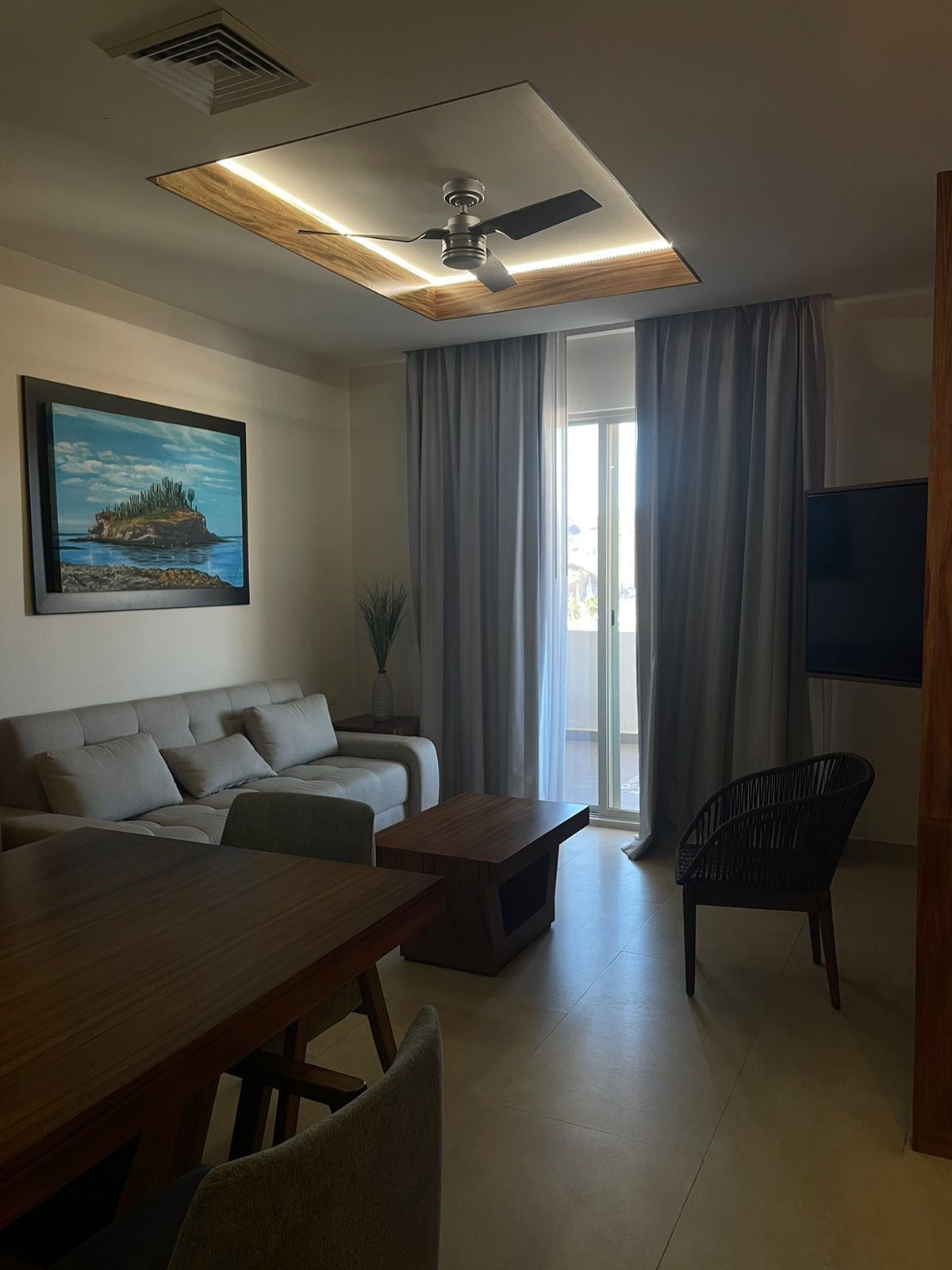 A modern living room with a sofa, coffee table, dining table, and a ceiling fan.