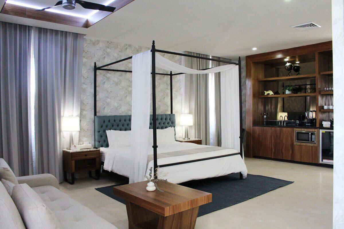 Une chambre d’hôtel moderne avec un lit à baldaquin, un canapé, une table d’appoint en bois et une kitchenette.