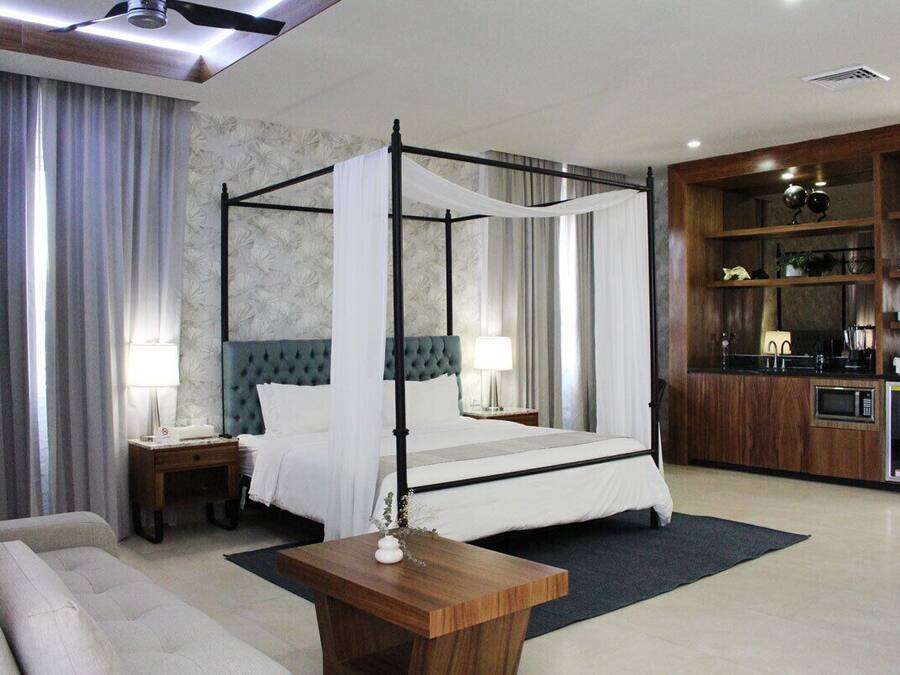 Een moderne hotelkamer met een hemelbed, een bank, een houten bijzettafeltje en een kitchenette.