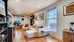 A spacious living room with a white sofa, a small table, and a bookshelf. - Quiet 2 BR near RiNo w/ sunroom & large backyard (Denver)