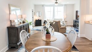 A dining area with a wooden table, white chairs, a dark wooden cabinet, and a mirror on the wall. - Stoney Ridge · Cozy 1st Level King Bed Suite - 2 bed 2 bath! (Forest)