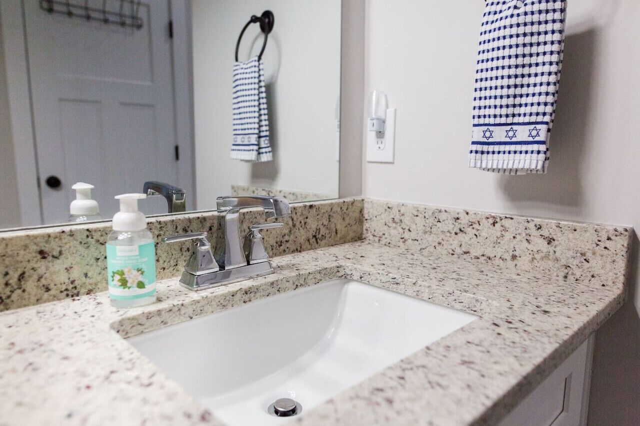 Une salle de bain avec un lavabo blanc, un miroir, un porte-serviettes sur lequel est posée une serviette bleue et blanche, et un flacon de savon pour les mains.