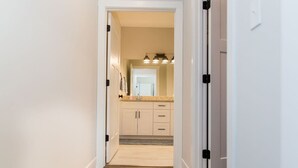 A hallway leading to a kitchen with light-colored cabinets, a granite countertop, and a mirror above the sink. - Stoney Ridge · Cozy 1st Level King Bed Suite - 2 bed 2 bath! (Forest)