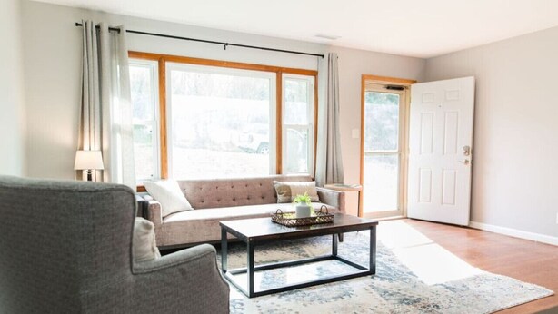 A living room with a sofa, armchair, coffee table, and a large window with curtains. - Charming Single Level Home • Convenient 3 Bedroom (Lynchburg)