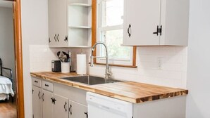 A modern kitchen with white cabinets, a wooden countertop, a built-in dishwasher, and a stainless steel trash can. - Charming Single Level Home • Convenient 3 Bedroom (Lynchburg)