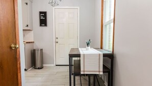 A hallway with a white door, a trash bin, a table with a white tablecloth, and a potted plant. - Charming Single Level Home • Convenient 3 Bedroom (Lynchburg)