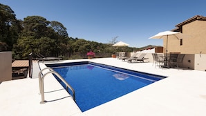 A rectangular swimming pool with a metal ladder on one side, surrounded by a white deck. There are outdoor chairs and a table with umbrellas. - Moderna Villa con Hermosa Vista al Lago (Valle de Bravo)