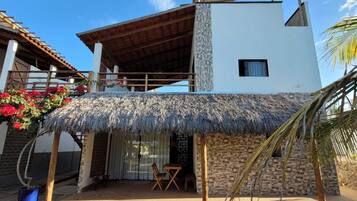 Un edificio moderno de dos pisos con un patio de techo de paja, un muro de piedra y una terraza de madera.