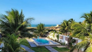 Zona de piscina con vista despejada al océano, rodeada de palmeras y una terraza de madera.