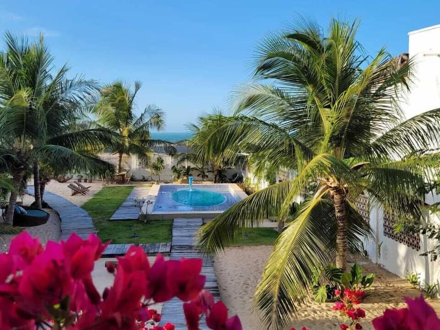 A pool area with palm trees, a wooden deck, and a view of the ocean.