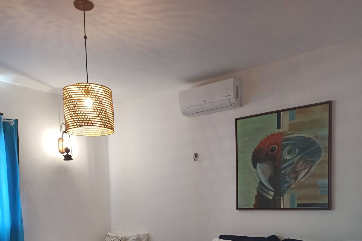 Une chambre d’hôtel comprenant un lit, un banc, un luminaire suspendu et un climatiseur fixé au mur.