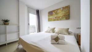 Un dormitorio con una cama grande, un cuadro en la pared, una ventana con cortinas y una planta sobre una estantería.