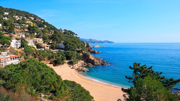 Una zona costera con playa de arena, costa rocosa y edificios residenciales en una colina.