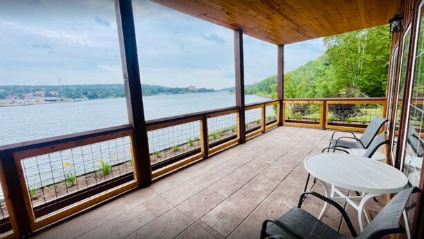 A covered outdoor area with a view of a river and hills. There are chairs and a table. - Riverbank Trailside Cabin 24A (Houghton)