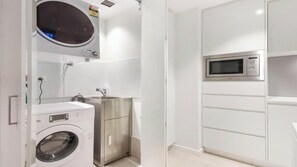 Pieni ja käytännöllinen pyykinhuoltotila, jossa on pyykinpesukone, pesuallas ja mikroaaltouuni.