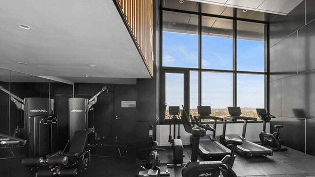 A modern gym with various exercise equipment, large windows, and a view of the city.