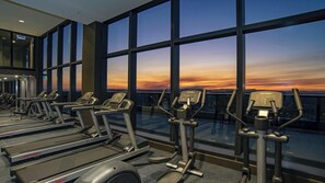 A gym with treadmills and elliptical machines, large windows with a sunset view. - Luxury 1 BDR Skytower City River Views (Brisbane City)