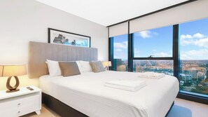 A modern hotel room with a large bed, a nightstand, a city view through large windows, and a framed picture on the wall. - Luxury 1 BDR Skytower City River Views (Brisbane City)