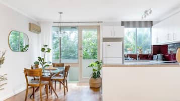 Une cuisine moderne avec des meubles blancs, un coin repas avec des chaises en bois et une vue sur la verdure à l’extérieur.