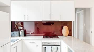 Une cuisine moderne avec des meubles blancs, un four encastré, une plaque de cuisson et un grille-pain.