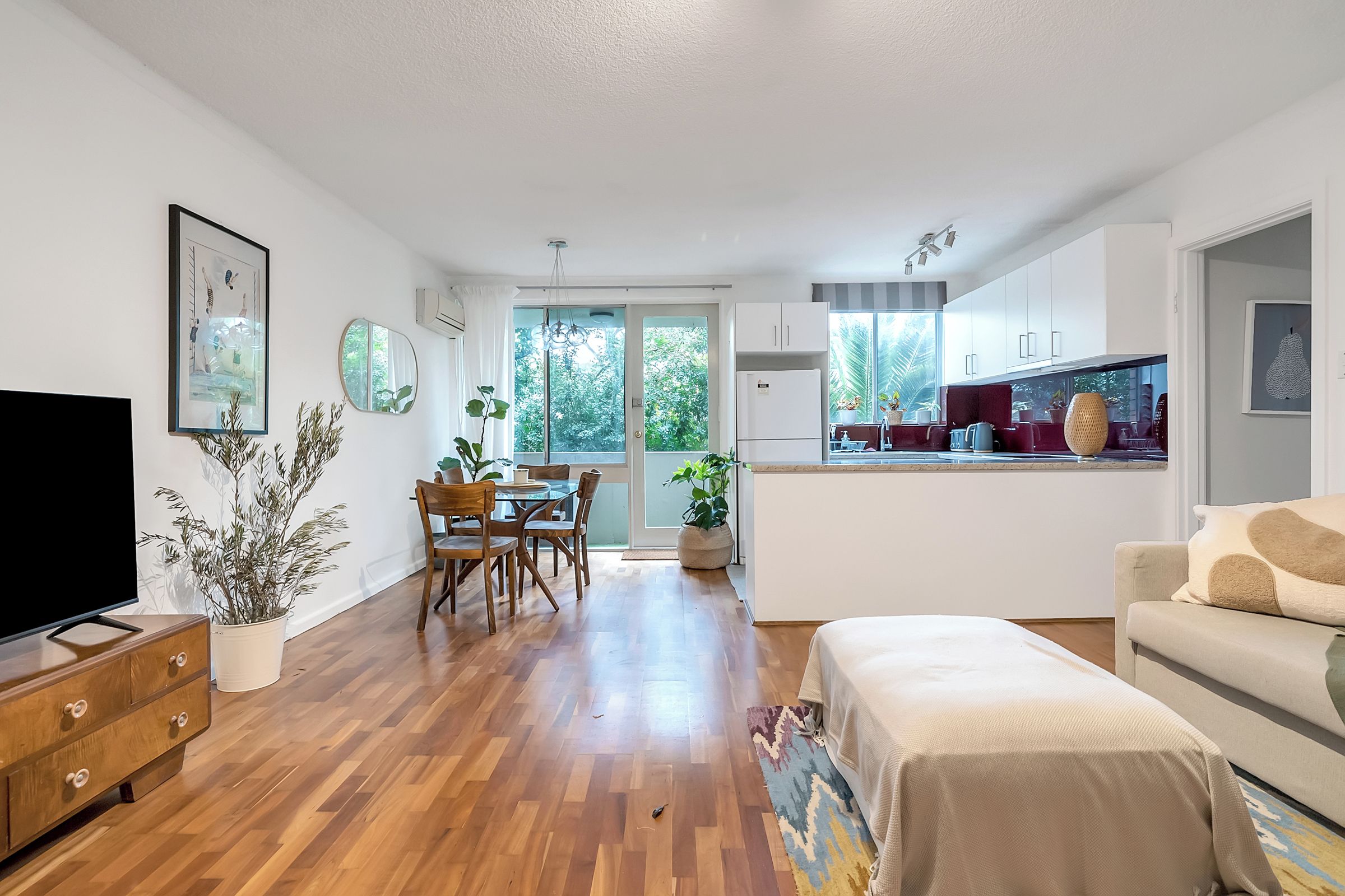 A modern living room with a TV, wooden furniture, and a dining area with a table and chairs.