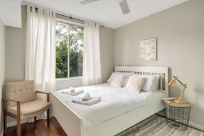 A bedroom with a bed, a chair, a bedside table with a lamp, and a window with curtains. - Cosy Bright 1 BDR Apt Lane Cove (Lane Cove)