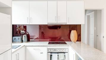 A modern kitchen with white cabinets, a built-in oven, a stovetop, and a toaster.