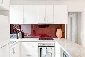 Une cuisine moderne avec des meubles blancs, un four encastré, une plaque de cuisson et un grille-pain.