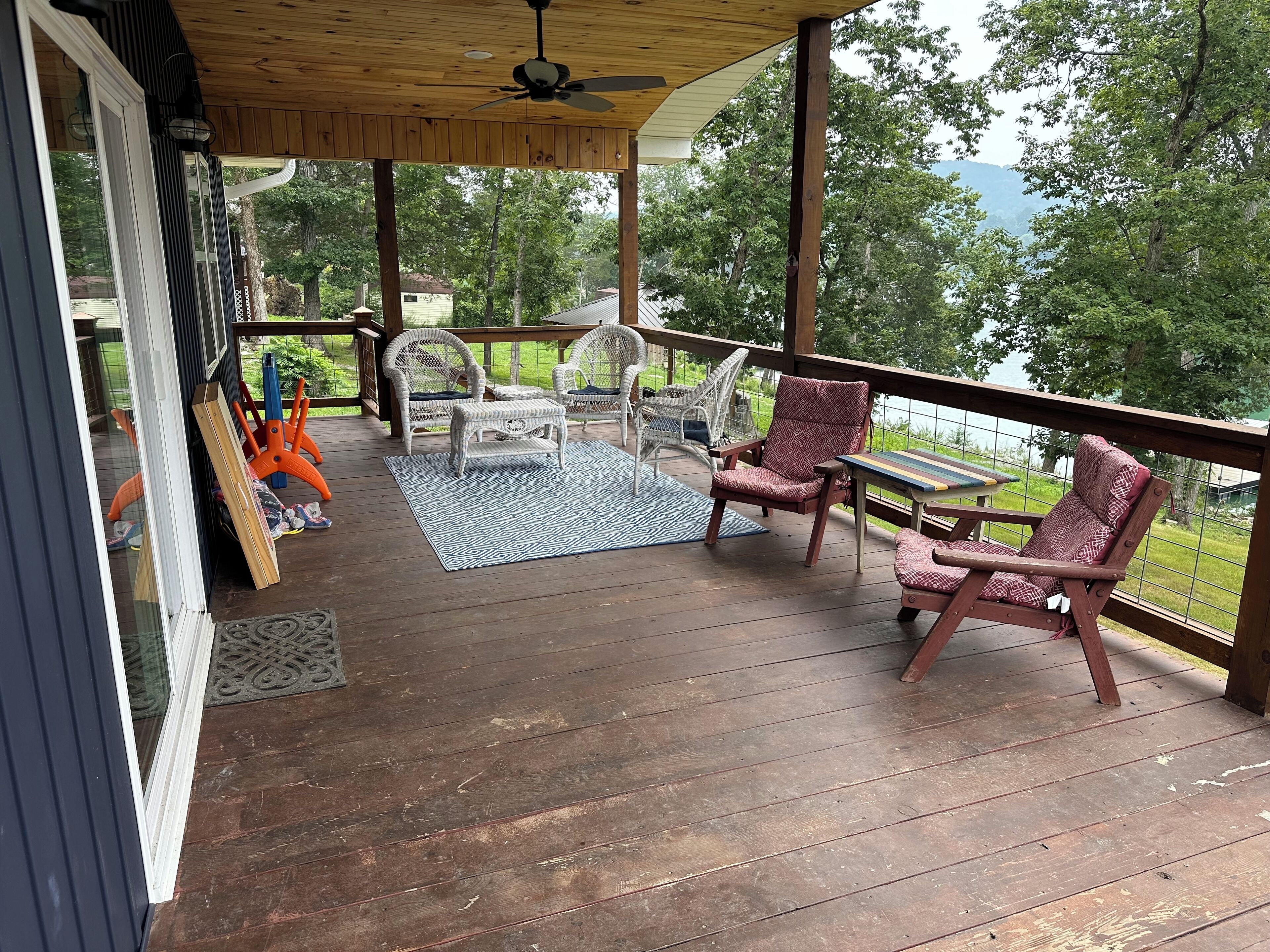 En overdækket terrasse med fletningsmøbler, et bord og udsigt over naturen.