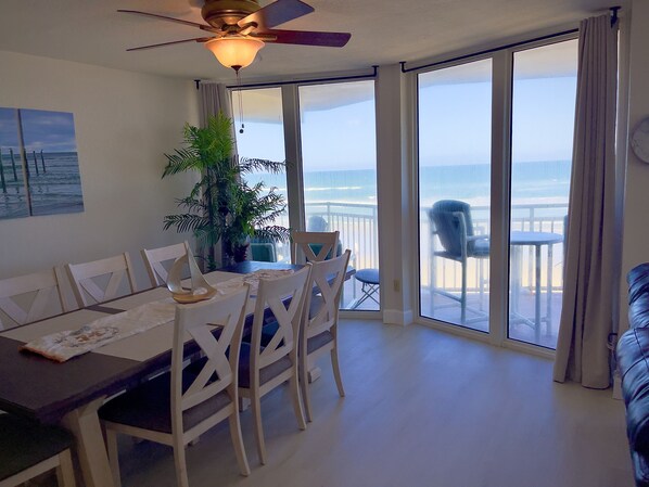 A dining area with a table, chairs, and a ceiling fan. There is a large window with a view of the ocean.