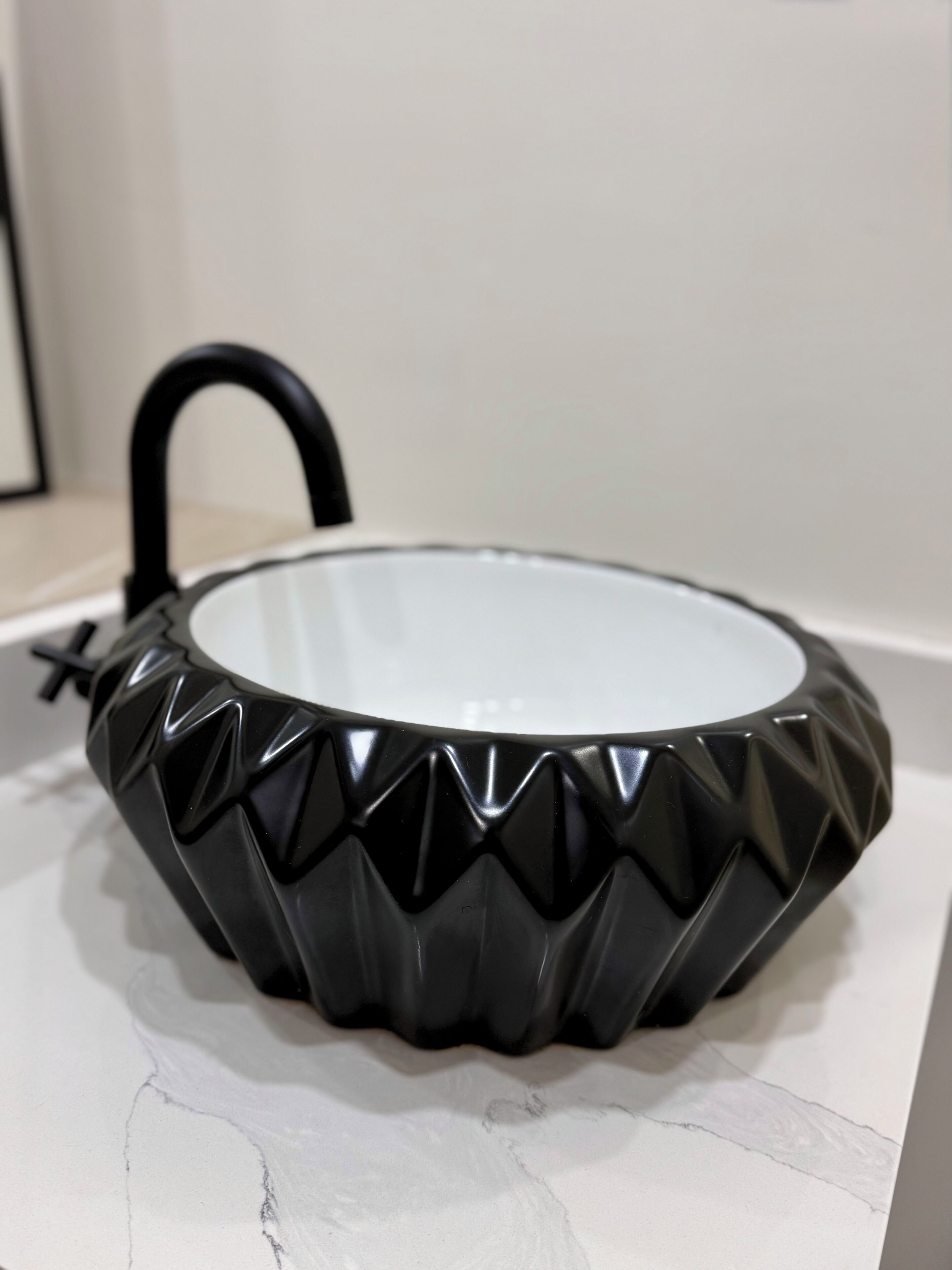 Un objet noir, à surface striée et de forme ronde, doté d’une anse, posé sur une surface blanche.