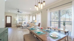 A spacious dining area with a long table set for a meal, large windows with blinds, and a ceiling fan. - Custom Coastal Getaway in the Heart of Long Beach, stroll to beach and dining (Long Beach,)