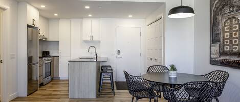 A modern kitchen with white cabinets, a central island, and black chairs around a dining table.