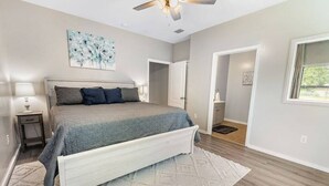 Una camera da letto con un letto, una ventola a soffitto, un quadro e una porta che dà su un'altra stanza.