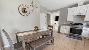 Una cucina moderna con mobili bianchi, forno integrato e zona pranzo con tavolo e sedie in legno.