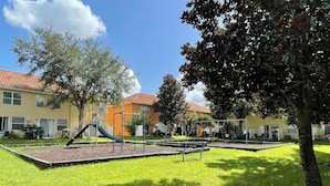 A playground with slides and swings, surrounded by grass and trees, with buildings in the background. - DISNEY R US! UNIVERSAL IS TOO!!! (Kissimmee)