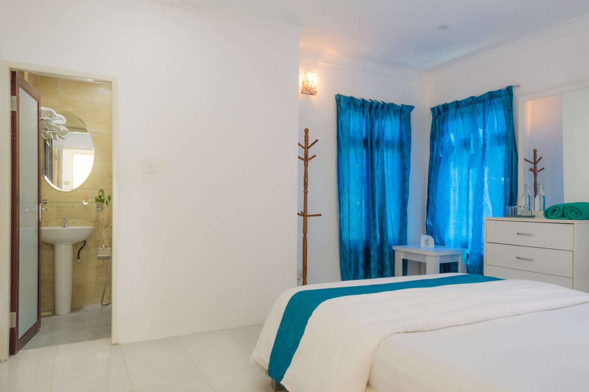 Un dormitorio con cama, mesita de noche, espejo, armario y baño con lavabo y espejo.