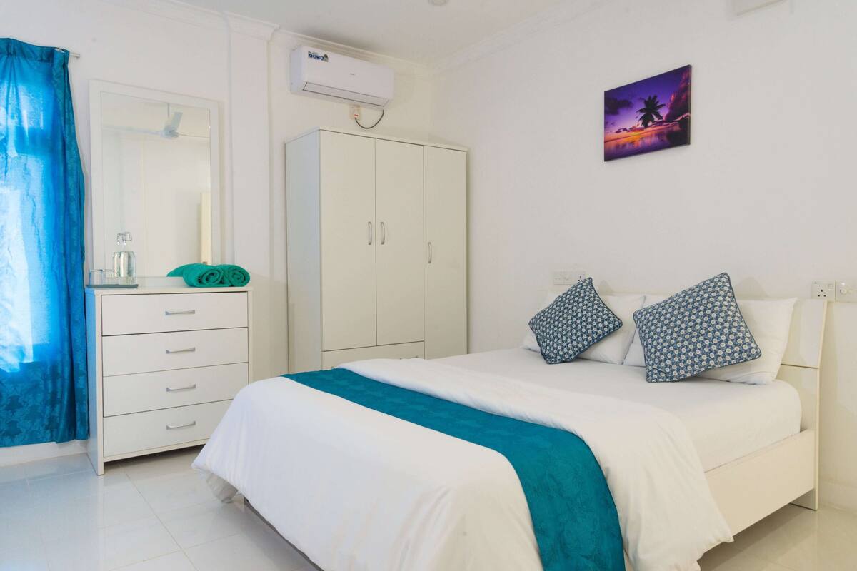 Habitación de hotel con cama, armario, espejo, lavabo y perchero.