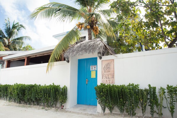 A building with a blue door, a palm tree, and a sign that reads "PALM GATE". - Palm Gate Maldives (Thulusdhoo Island)