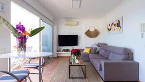 A modern living room with a grey sofa, a TV mounted on the wall, and a dining area with a table and chairs. - Tufia Marine Life by Canariasgetaway (Telde)
