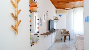 A living room with a TV on a wooden stand, a chair, and a mirror with colorful decorations.