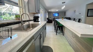 A modern kitchen with a large island, stainless steel appliances, and a dining area with bar stools. - Poolside Cocoa Oasis with Tiki Bar (Port Saint John)