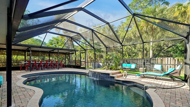 A covered outdoor swimming pool with a brick edge, lounge chairs, and a barbecue area. - Poolside Cocoa Oasis with Tiki Bar (Port Saint John)