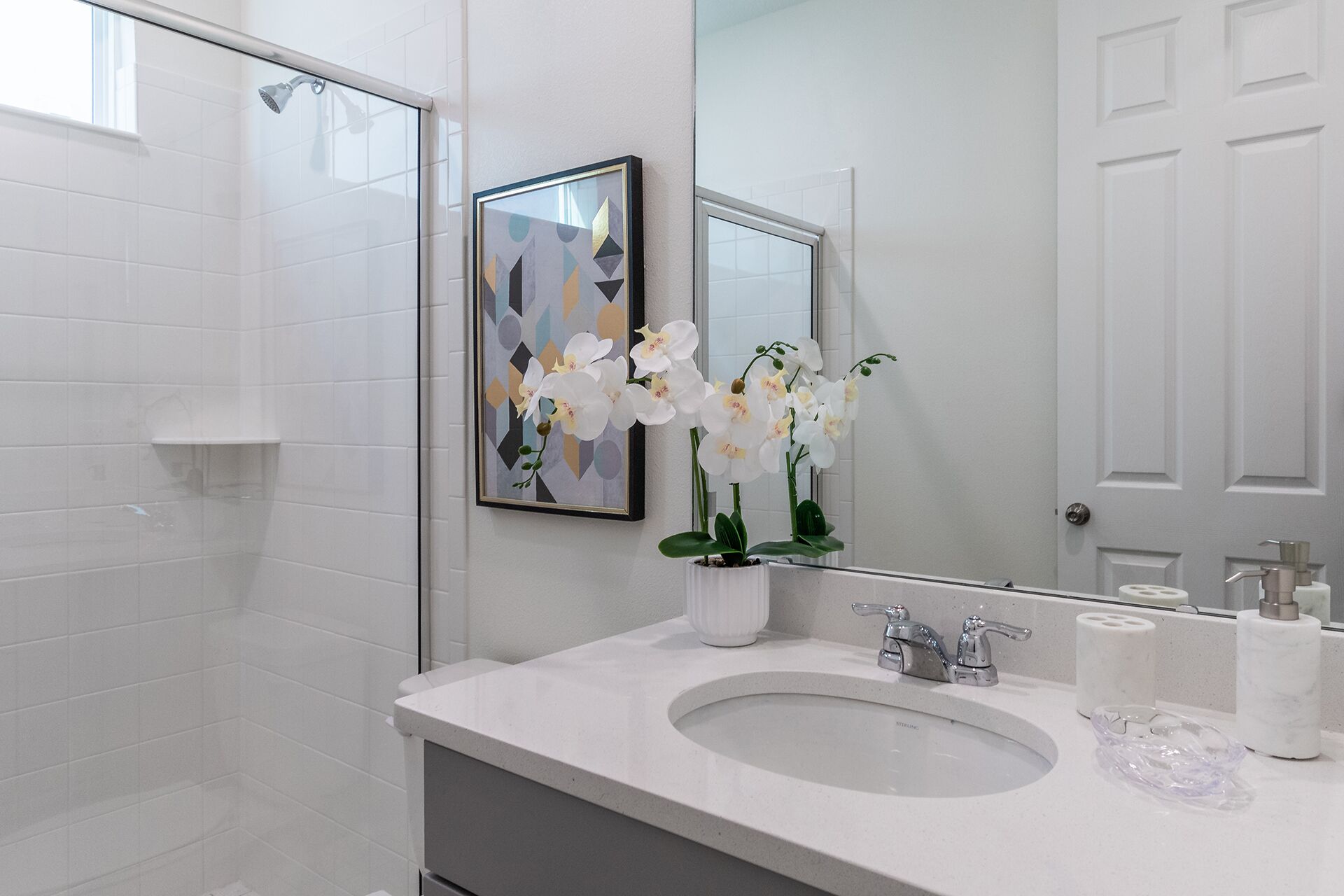 Un baño con un lavamanos blanco, un espejo y un cuadro abstracto enmarcado.