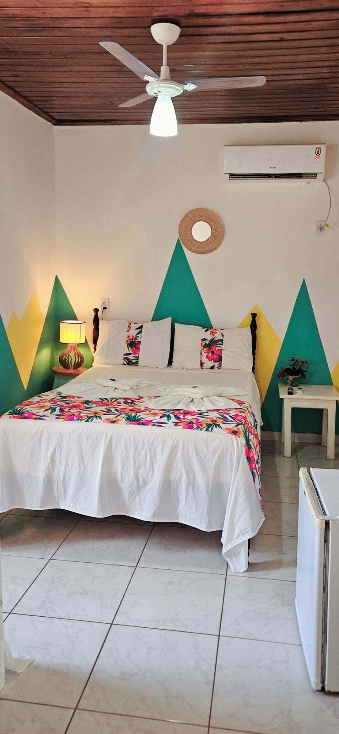 A bedroom with a bed, a ceiling fan, an air conditioner, and a small table.