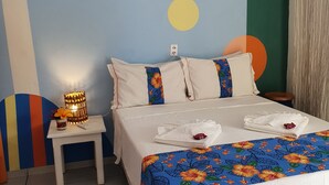 Habitación de hotel con cama, almohadas, mesita de noche, lámpara y una pared decorada con arte abstracto.