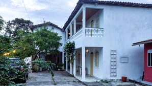 Un edificio de dos pisos con un balcón, un patio empedrado de piedra y plantas en macetas.
